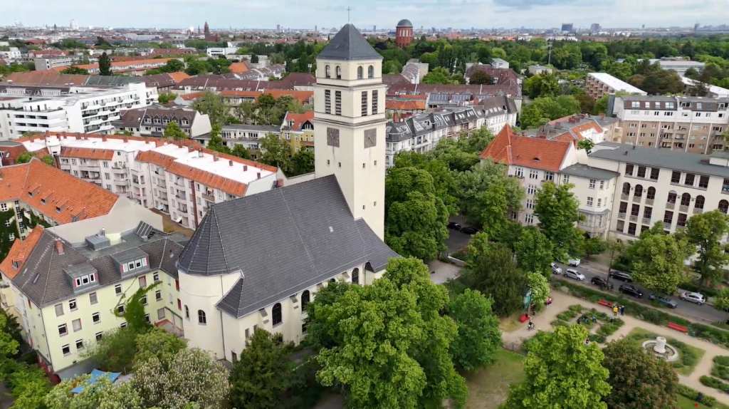 Luftaufnahme von Markuskirche mit regenwasserspendendem Kirchendach und daneben gelegenem Markusplatz